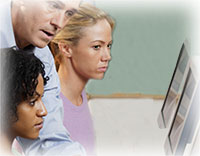 Photo of girl at computer looking at another's monitor